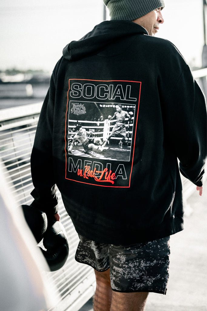 The back side of the Social Media vs Real Life Fight hoodie worn by a model walking down a bridge. 